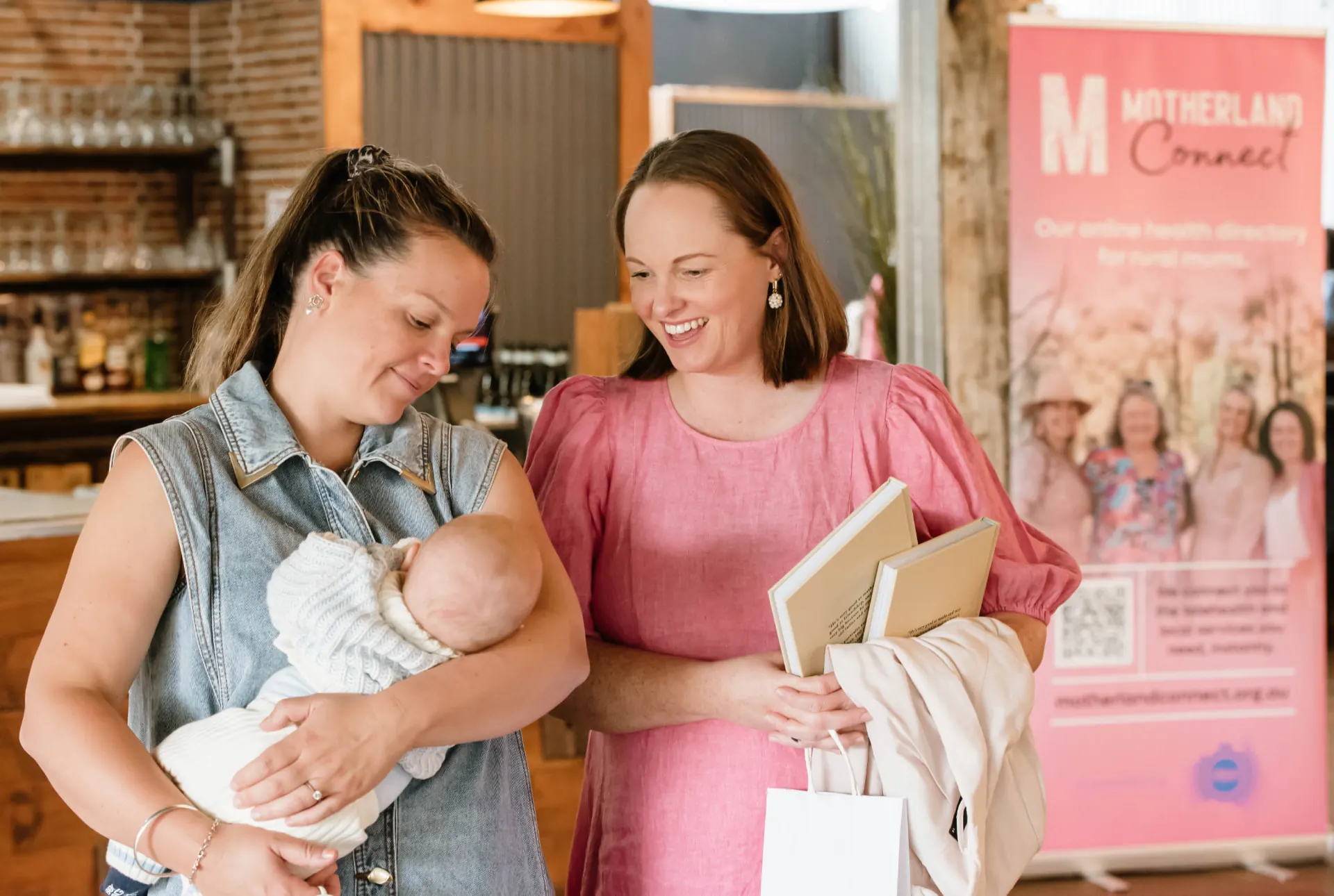 A mum holding her newborn, chatting with a Motherland team member at a community event