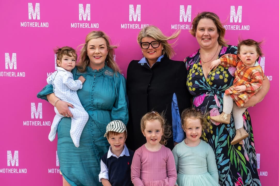 Motherland mums and their children in front of a pink Motherland wall
